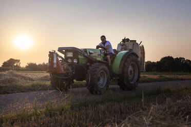 Biobauer auf einem Traktor bei Sonnenuntergang - SEBF00207