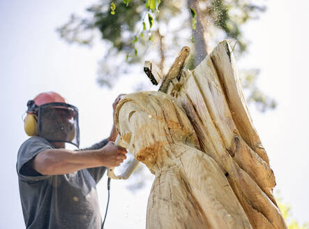 Wood carver carving angel sculpture, using chainsaw - BFRF02067