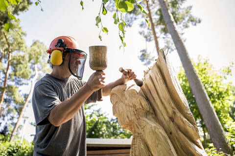 Holzschnitzer beim Schnitzen einer Skulptur mit Meißel, lizenzfreies Stockfoto