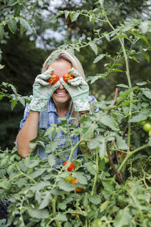 Blonde lächelnde Frau bei der Tomatenernte, Tomaten auf den Augen - HMEF00523
