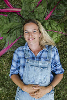Blonde Frau bei der Ernte von Gemüse aus ihrem Hochbeet in ihrem eigenen Garten - HMEF00537