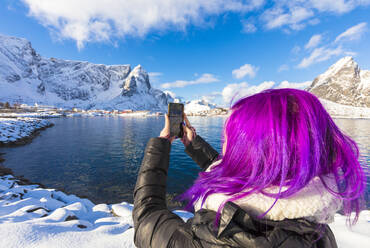 Woman with fuchsia hair taking photo with smartphone, Reine Bay, Lofoten Islands, Nordland, Norway, Europe - RHPLF09233