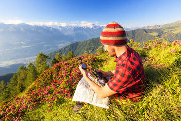 Wanderer sitzt in der Nähe von Rhododendren auf dem Pizzo Berro und schaut auf den Kompass und die Karte, Bitto-Tal, Lombardei, Italien, Europa - RHPLF09235