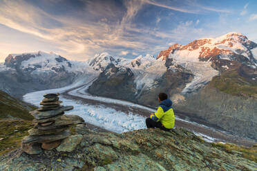 Hiker sitting on rocks looking towards Monte Rosa glacier, Zermatt, canton of Valais, Swiss Alps, Switzerland, Europe - RHPLF09248