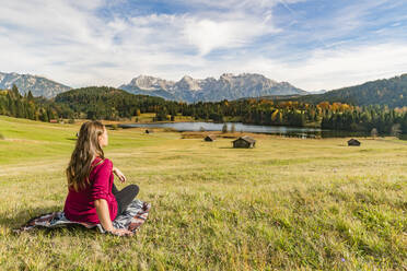 Frau sitzt und starrt auf den Geroldsee und die Karwendelalpen, Krun, Oberbayern, Bayern, Deutschland, Europa - RHPLF09263