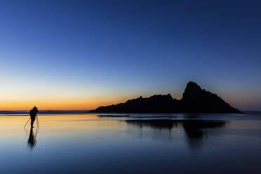 Tourist beim Fotografieren am Strand von Karekare gegen den klaren Himmel bei Sonnenuntergang, Neuseeland - FOF10909