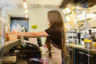 Junge Frau arbeitet an der Theke eines Cafés - GIOF07053