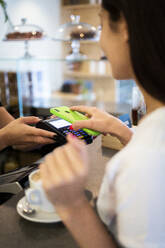 Nahaufnahme eines Kunden, der in einem Café bargeldlos mit seinem Smartphone bezahlt - GIOF07057