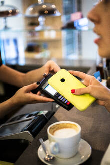 Nahaufnahme eines Kunden, der in einem Café bargeldlos mit seinem Smartphone bezahlt - GIOF07058