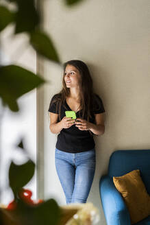 Junge Frau lehnt an einer Wand und hält ein Mobiltelefon in der Hand - GIOF07062