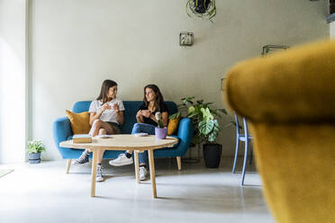 Zwei junge Freundinnen sitzen auf einer Couch in einem Café und unterhalten sich - GIOF07070