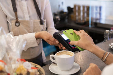 Nahaufnahme eines Kunden, der in einem Café bargeldlos mit seinem Smartphone bezahlt - GIOF07082