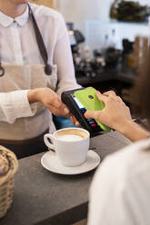 Nahaufnahme eines Kunden, der in einem Café bargeldlos mit seinem Smartphone bezahlt - GIOF07083