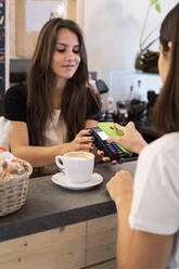 Customer paying cashless with smartphone in a cafe - GIOF07084