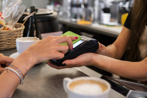 Nahaufnahme eines Kunden, der in einem Café bargeldlos mit seinem Smartphone bezahlt - GIOF07086