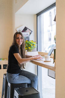 Lächelnde junge Frau mit Laptop in einem Cafe - GIOF07088