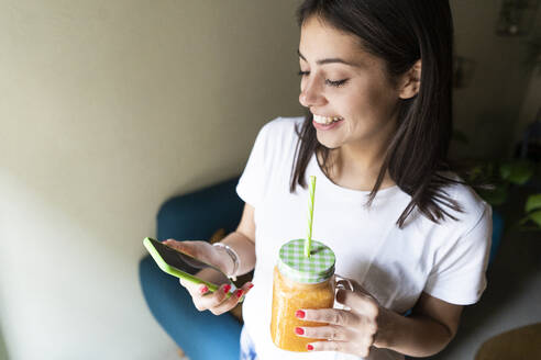 Glückliche junge Frau mit einem Smoothie und einem Mobiltelefon in einem Café - GIOF07099
