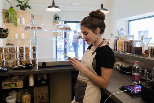 Young woman using cell phone behind the counter in a cafe - GIOF07102