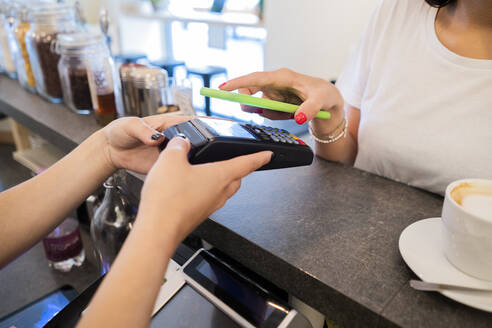 Nahaufnahme eines Kunden, der in einem Café bargeldlos mit seinem Smartphone bezahlt - GIOF07104