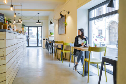 Junge Frau mit Mobiltelefon in einem Café sitzend, lizenzfreies Stockfoto