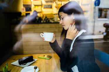 Junge Frau in einem Café hinter der Fensterscheibe - GIOF07109