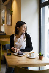 Lächelnde junge Frau in einem Cafe, die aus dem Fenster schaut - GIOF07111