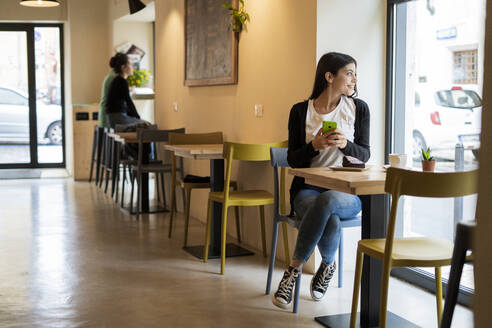 Lächelnde junge Frau in einem Cafe, die aus dem Fenster schaut - GIOF07113