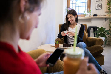 Zwei junge Frauen sitzen in Sesseln in einem Cafe - GIOF07114