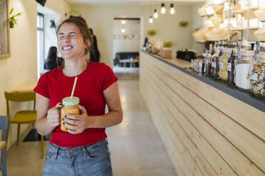 Glückliche junge Frau mit einem Smoothie in einem Café - GIOF07124