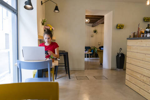 Junge Frau mit Handy und Laptop in einem Cafe, lizenzfreies Stockfoto