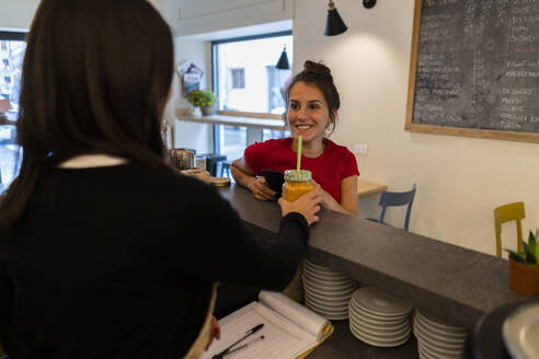 Lächelnde junge Frau an der Theke eines Cafés - GIOF07138