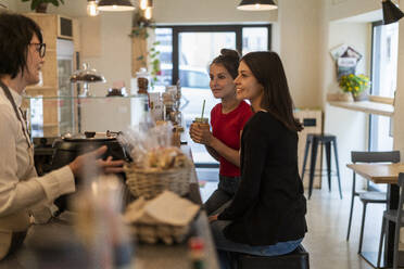 Two young female friends in a cafe talking with barista - GIOF07140