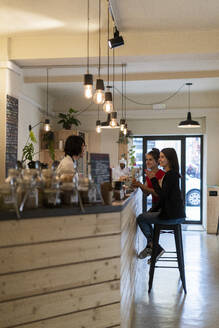 Zwei junge Freundinnen in einem Café im Gespräch mit dem Barista - GIOF07141