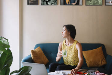 Fashion designer sitting on couch having a break and drinking flavoured water - ALBF01119