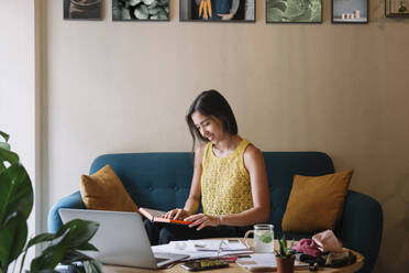 Smiling fashion designer sitting on couch working on a new collection - ALBF01127