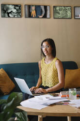 Porträt einer lächelnden Modedesignerin, die auf einer Couch sitzt und einen Laptop benutzt - ALBF01131