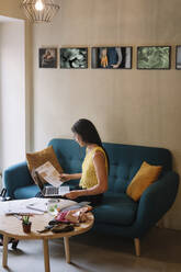 Fashion designer sitting on couch checking color samples - ALBF01133