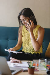 Smiling fashion designer sitting on couch talking on the phone - ALBF01140