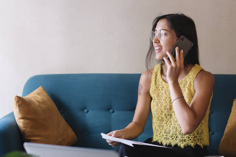 Smiling young woman sitting on couch talking on the phone stock photo