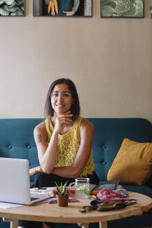 Portrait of smiling fashion designer sitting on couch - ALBF01149