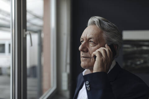 Portrait of a senior businessman talking on cell phone at the window stock photo