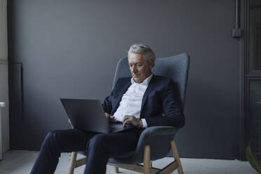 Älterer Geschäftsmann im Sessel sitzend mit Laptop - GUSF02616