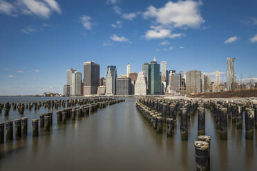 Holzpfähle im East River mit modernen Gebäuden im Hintergrund gegen den Himmel, New York City, USA - XCF00217