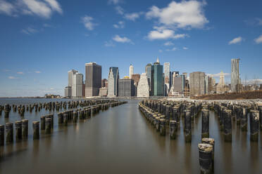 Wooden posts in East river with modern buildings in background against sky, New York City, USA - XCF00217