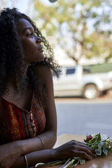 Porträt einer jungen afrikanischen Frau mit Blumen auf dem Tisch in einem Café, Blick aus dem Fenster - VEGF00689