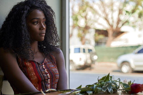 Porträt einer jungen afrikanischen Frau mit Blumen auf dem Tisch in einem Café, Blick aus dem Fenster - VEGF00690
