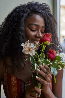 Porträt einer jungen afrikanischen Frau, die in einem Café an Blumen riecht und lächelt - VEGF00691