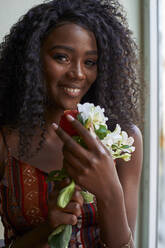 Porträt einer jungen afrikanischen Frau mit Blumen in der Hand und einem Lächeln in einem Café - VEGF00692