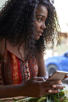 Porträt einer jungen afrikanischen Frau in einem Café, die ihr Smartphone überprüft - VEGF00693