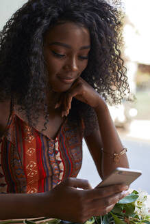 Porträt einer jungen afrikanischen Frau in einem Café, die ihr Smartphone überprüft - VEGF00694